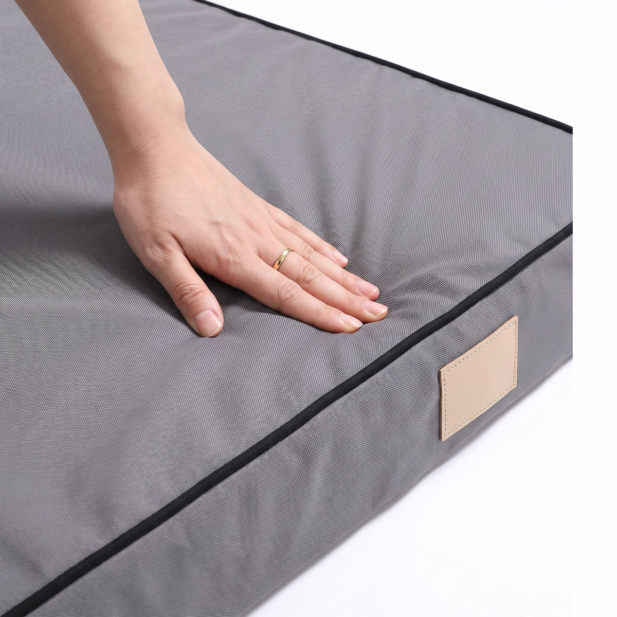 Close-up of a hand pressing into the Oxford cover of the foam dog mattress near the piped edge
