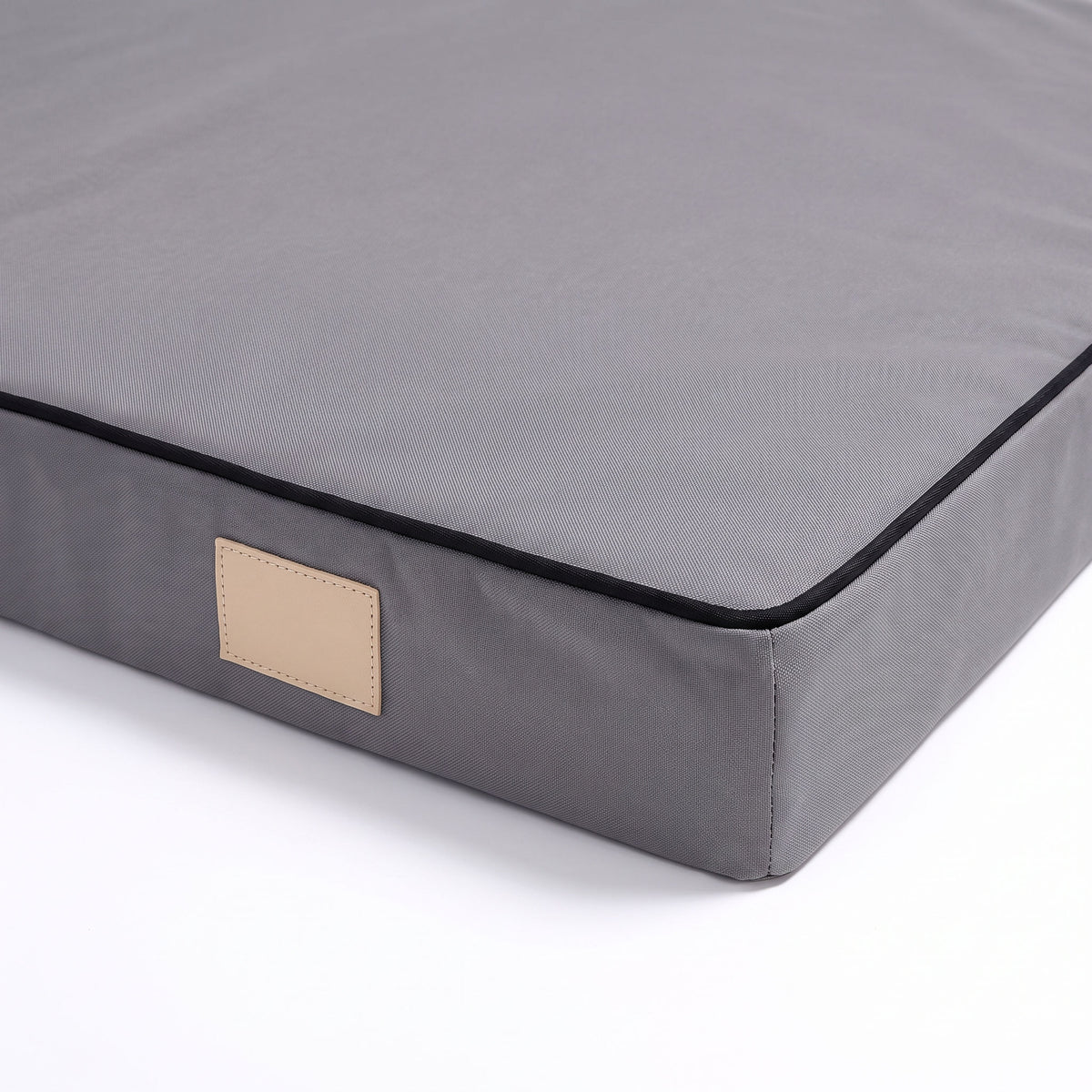 Close detail of the flat foam dog mattress corner on a white background, showing the black piped border and beige tag
